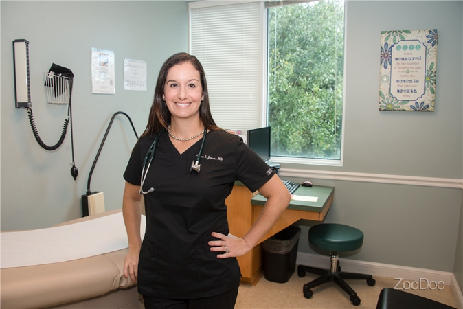 Dr. Megan Janson standing and smiling in Patient Room. She is wearing a stethoscope around her neck.